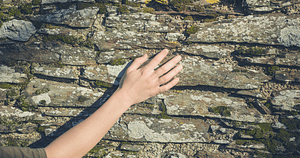 On voit une main touchant un vieux mur en pierre